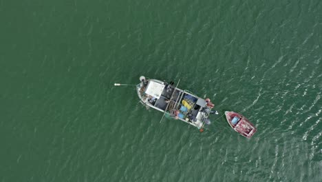 fishermen working on a small fishing boat lying in the green waters of salema, portugal