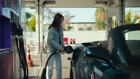 A-happy-girl-in-a-denim-jacket-refuels-her-gray-dark-convertible.-Stop-at-a-gas-station-to-fill-up-your-car