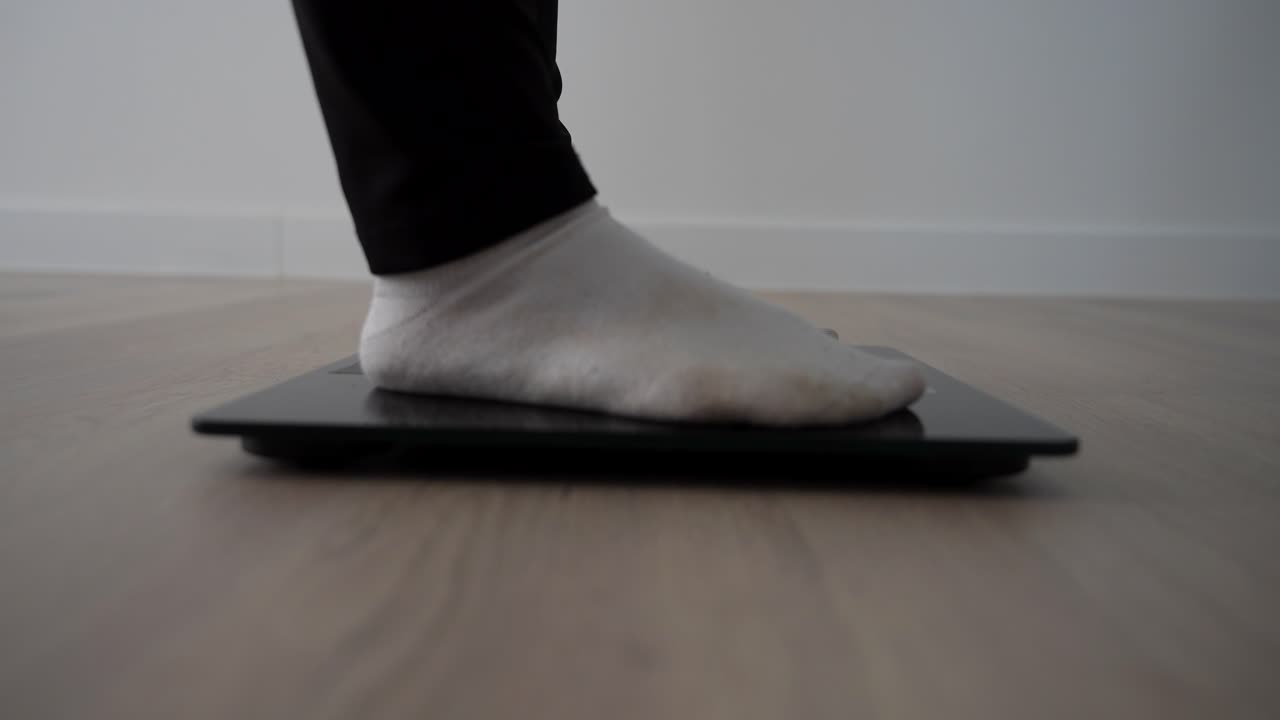 Profile shot of female feet stepping on digital scale to check weight on wooden floor
