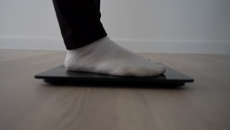 profile shot of female feet stepping on digital scale to check weight on wooden floor
