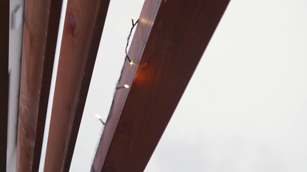 A Christmas light chain being hung up on a gloomy November day while it rains lightly. The lights are off at first, moved gently, then switch on, contrasting with the cold, grey atmosphere