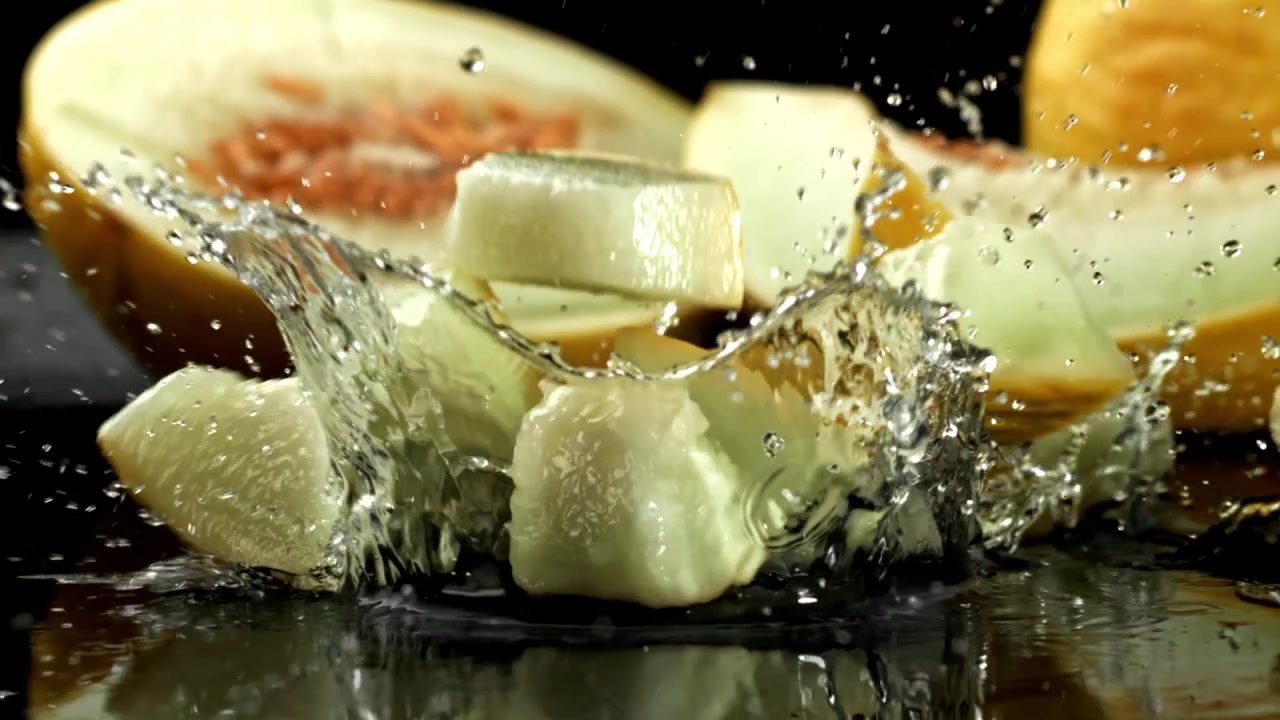 Pezzi di melone fresco che cadono nell'acqua con schizzi al rallentatore.