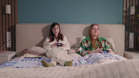 two girls playing video games in bed