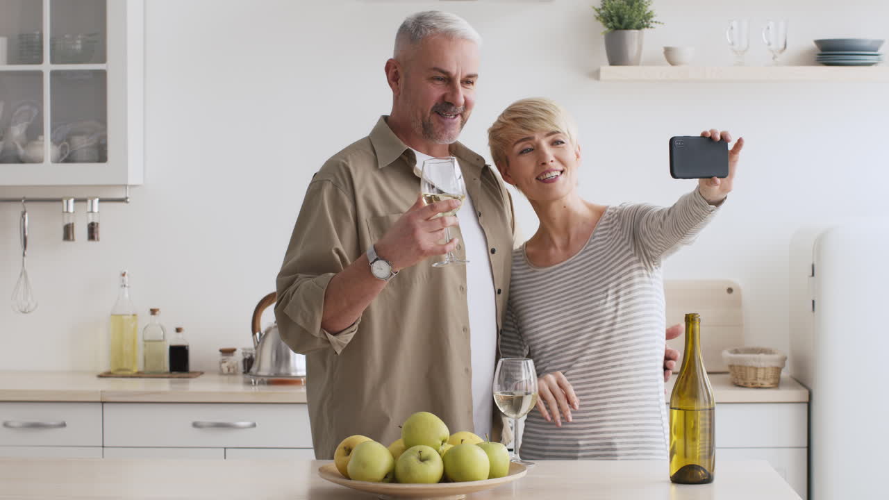 Coppia felice che si fa un selfie in videochiamata con vino in cucina