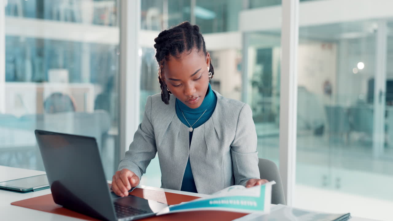 Smiling black entrepreneur working on financial reports at her desk in the office there are people in the background | Free Photo
