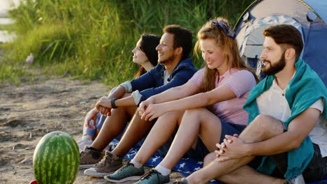 group of best friends multiethnic have a good time together at the sunset beside the lake they sitting beside of the tent and have a good conversation smiling and feeling relaxed