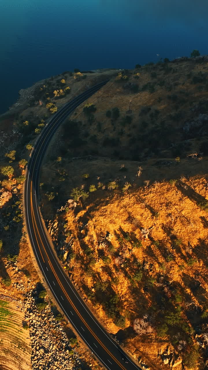 Highway going around the mountain in the picturesque scenery of California desert. Calm waters of lake around the rock. Top view. Vertical video