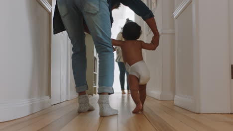 baby taking first steps learning to walk with mother and father teaching toddler at home enjoying parenthood