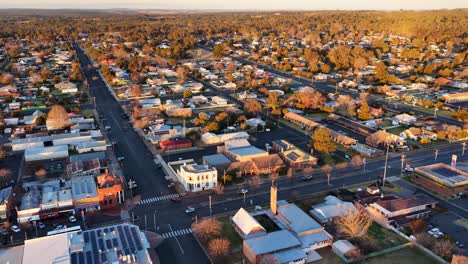 drone camera glides above coonabarabran, nsw at sunset, revealing grid-like streets, residential houses, and warm golden lighting in a wide aerial view