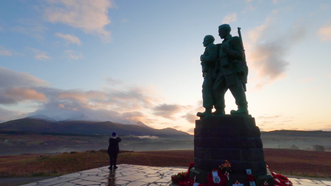 una mujer tomando fotografías del paisaje desde el memorial del comando en escocia durante la puesta de sol a medida que la cámara se acerca