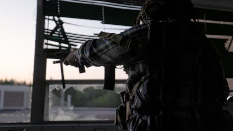 Silhouette-of-Soldier-with-Rifle-Sits-Armed-inside-building-takes-aim-out-Broken-Window-with-Automatic-Rifle-in-Tactical-Operation-Gear-and-Helmet