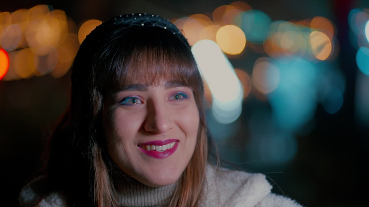 Close up of a young beautiful woman's Face smiling with the colourful Christmas Lights bokeh from Christmas Market in the background during a cold winter night in slow motion
