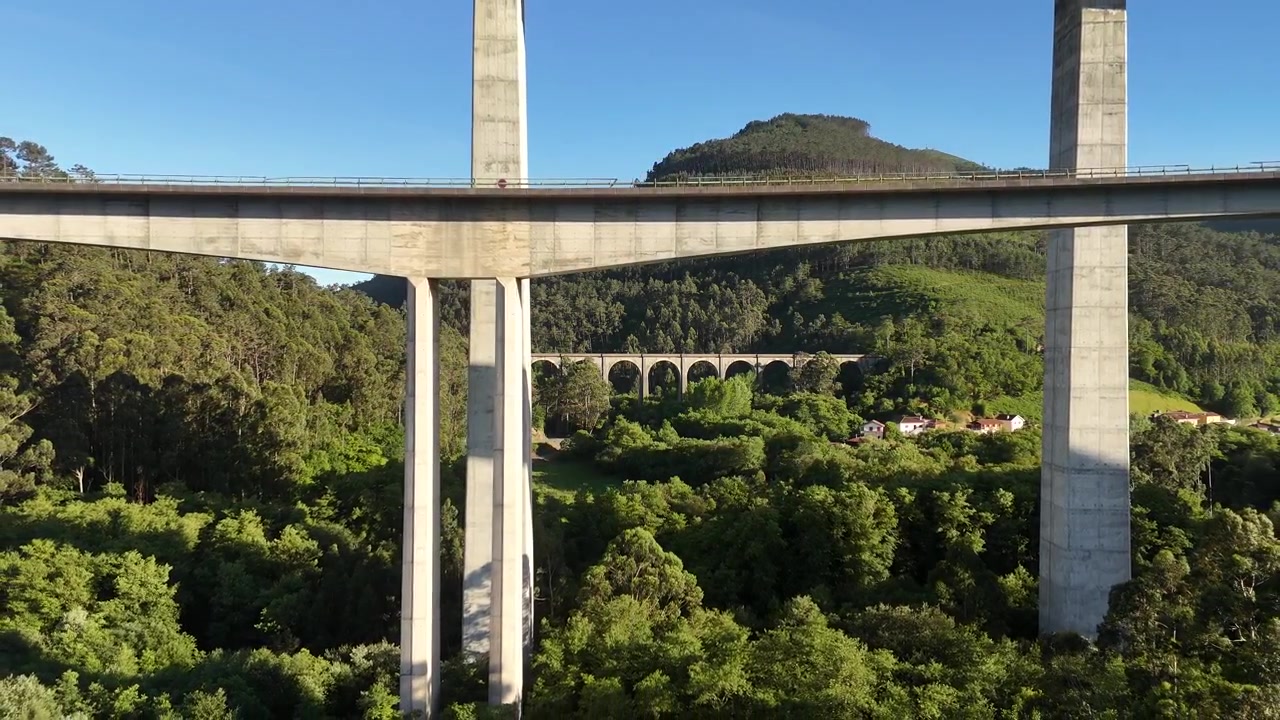 Drone che arretra per rivelare i viadotti di La Concha de Artedo su una valle boscosa