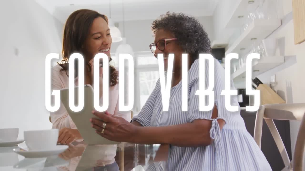 Animation of good vibes text over two women using tablet and smiling at home