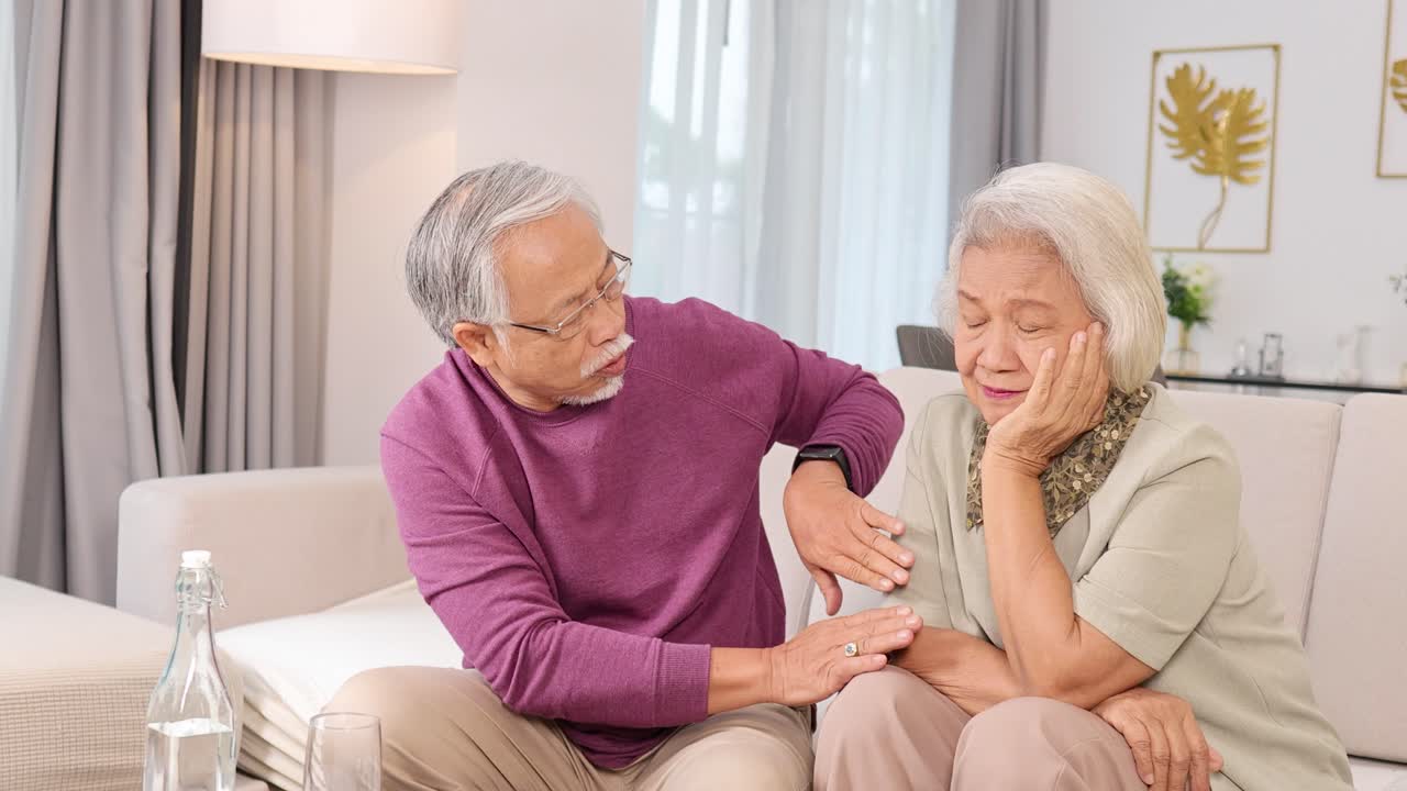 Elderly Asian couple sharing a tender, comforting moment together on a cozy sofa at home