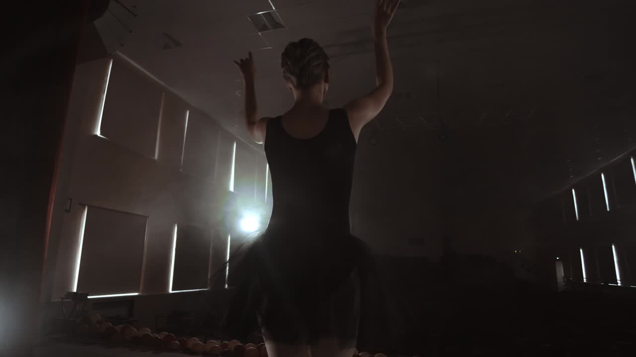 느린 동작: 무대 위의 프리마 발레가 콘트라의 어두운 빛 속에서 공연을 연습합니다.