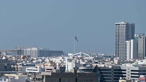 4k: the flag of the united arab emirates waving in the air over dubai city