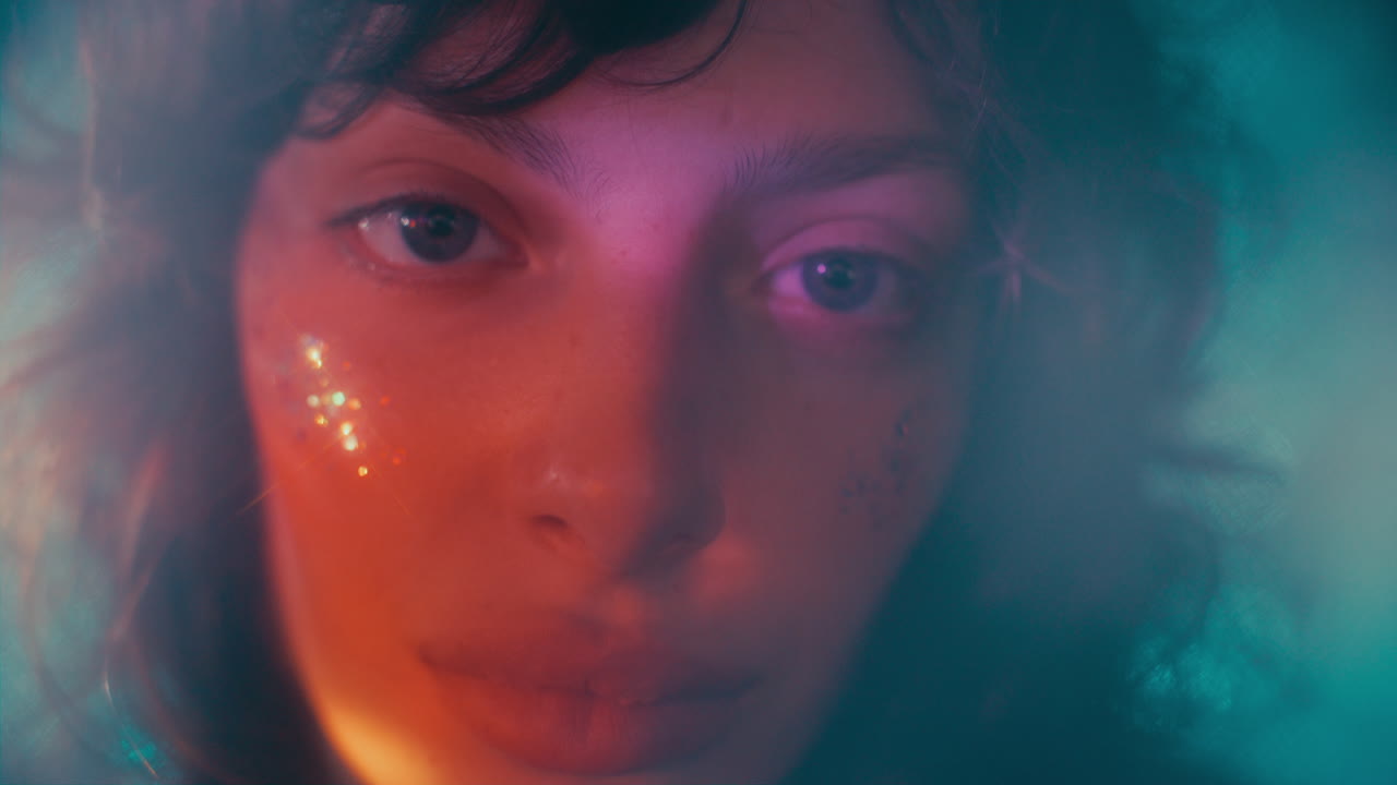 Portrait of Beautiful Girl with Glitter on Her Face in Soft Colorful Lighting