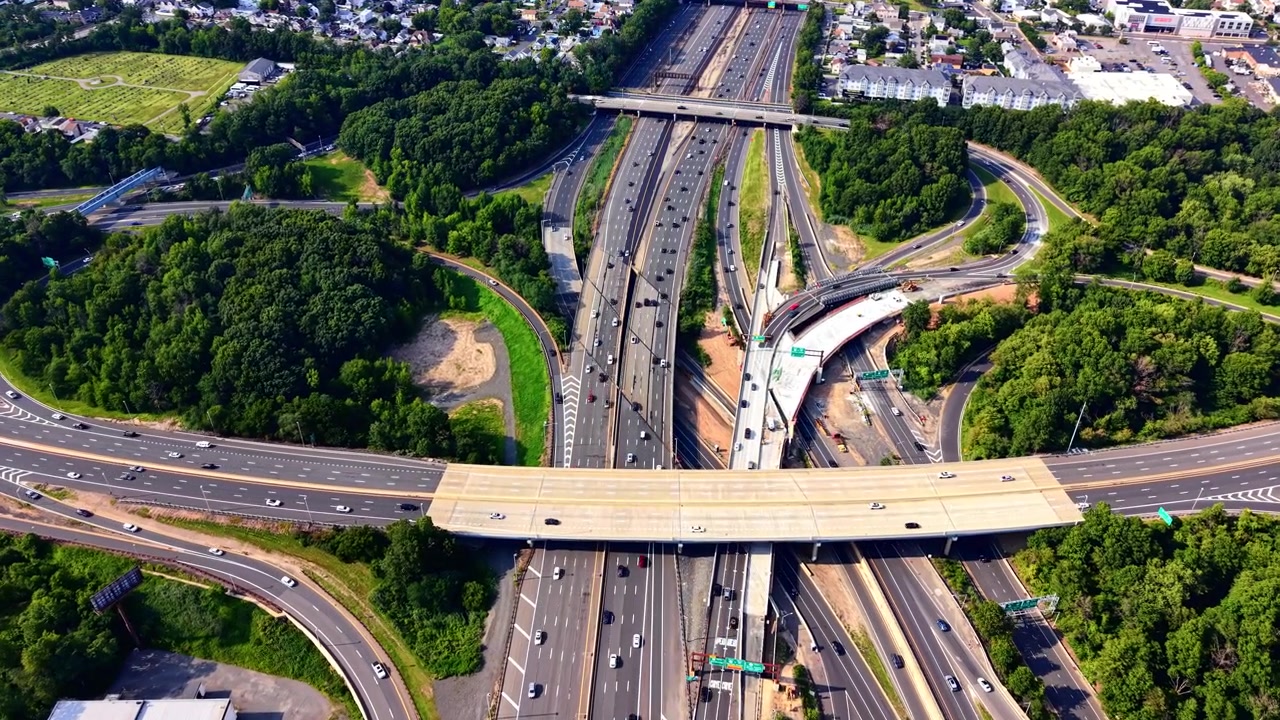 Highway intersection with multi lane roads and trees, United States. Drone perspective of asphalt route network surrounded by dense green forest under bright daylight. Garden State Parkway