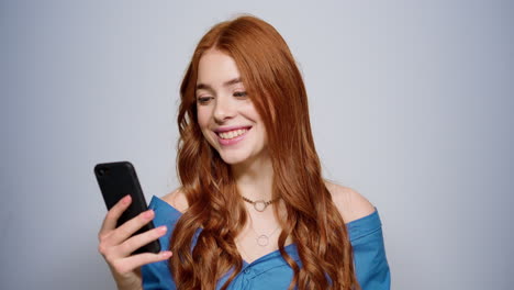 redhair girl holding mobile phone in studio. woman getting good news indoors