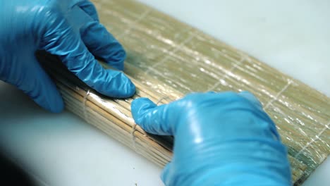 Close-up of professional chef's hands rolling a sushi roll on seaweed mat