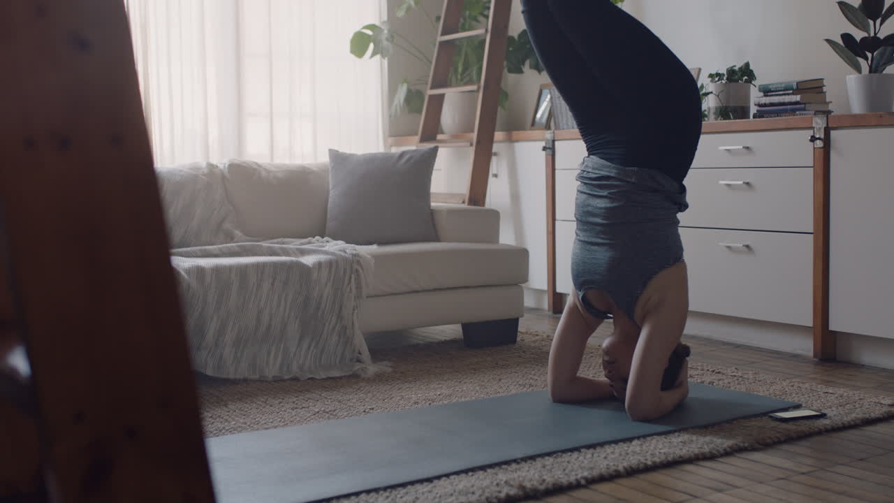 mujer de yoga saludable haciendo ejercicio en casa practicando postura de parada de cabeza apoyada en la sala de estar disfrutando del entrenamiento físico matutino