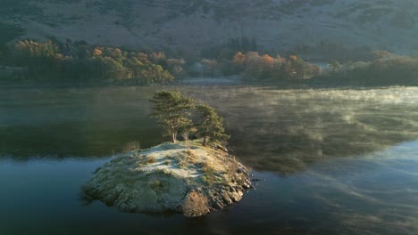 isla en un lago muy tranquilo mientras una suave niebla pasa por la superficie al amanecer en otoño