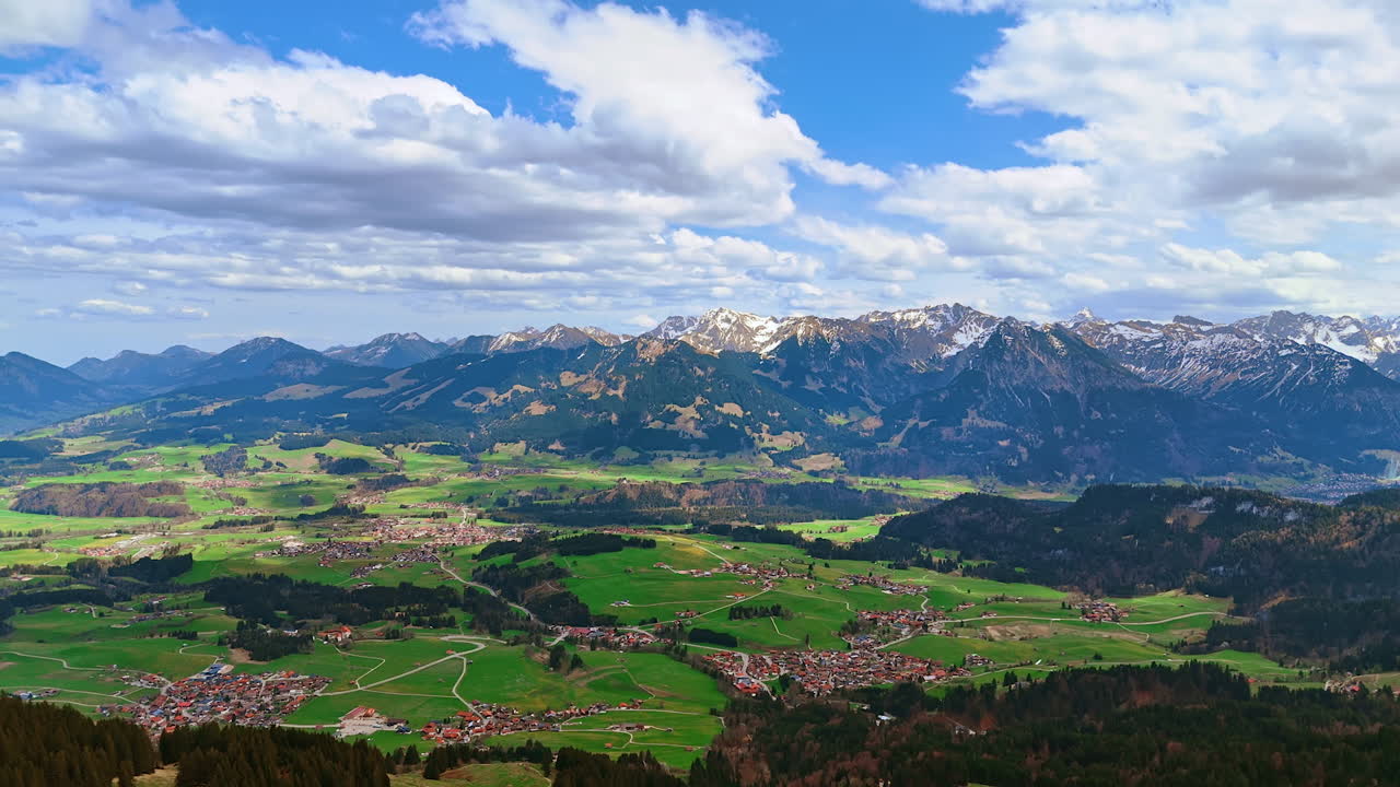 Picturesque valley among the stunning mountains with some snow on tops. Scenery of Bolsterlang, Bavaria, Germany from aerial perspective. Fluffy clouds in the blue sky.