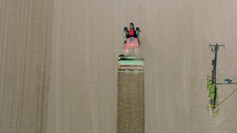 Vista-Aérea-Del-Campo-Arado-Con-Tractor-Sembrando-Semillas-De-Trigo,-Tema-Agrícola,-Tractor-Agrícola-Y-Sembradora-Plantando-Cultivos-En-Un-Campo-En-El-Soleado-Día-De-Primavera,-Tiro-De-Drones-De-Ojo-De-Pájaro-Avanzando