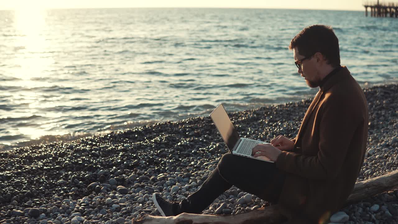 hombre trabajando en una computadora portátil en la playa al atardecer