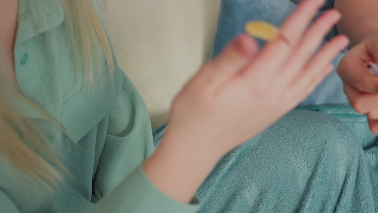 Close up of two people playfully pulling gummy candy from opposite ends while sitting on bed covered with blue blanket, showcasing fun interaction, lighthearted energy, and friendship moment