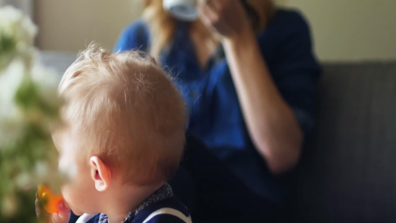 мальчик играет с игрушкой, в то время как мать пьет кофе на заднем плане 4k