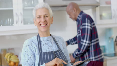 Retrato-De-Una-Feliz-Pareja-Birracial-Mayor-Cocinando-Y-Usando-Una-Tableta-En-La-Cocina,-Cámara-Lenta