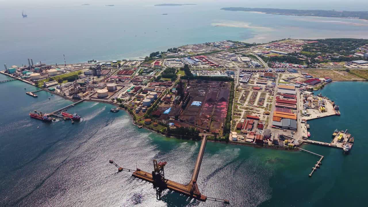 Slow drone shot of the Rancha-Rancha Industrial Estate in Labuan, Malaysia, showcasing a steel mill and sponge iron plant near the coastline under bright daylight