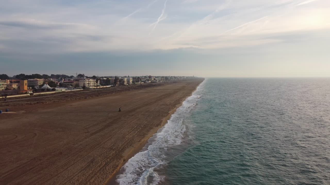 Castelldefels Beach in Barcelona, capturing the expansive sandy shore and waves gently lapping at the beach, quiet morning, aerial view