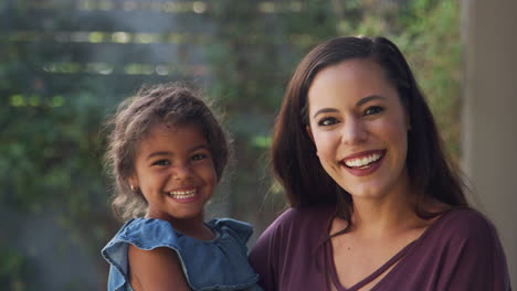 portrait of smiling hispanic mother with daughter laughing in garden at home