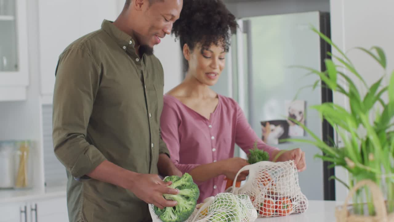 feliz pareja afroamericana con bolsas de verduras en la cocina