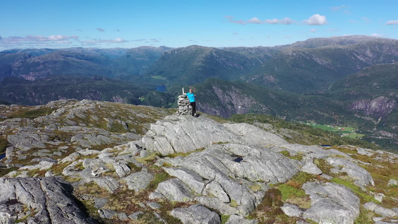 hombre parado en el pico de la montaña noruega en un clima soleado de verano - antena en movimiento hacia atrás de la persona mientras revela un paisaje montañoso masivo en el fondo - stamneshella vaksdal noruega