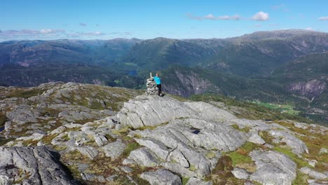 man standing on norwegian mountain peak in sunny summer weather - backward moving aerial from person while revealing massive mountain scenery in background - stamneshella vaksdal norway