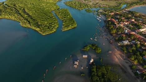 aerial pedestal view of a small village on the coast of brazil on the edge of a small delta with red roofed buildings and small fishing boats anchored off the coast