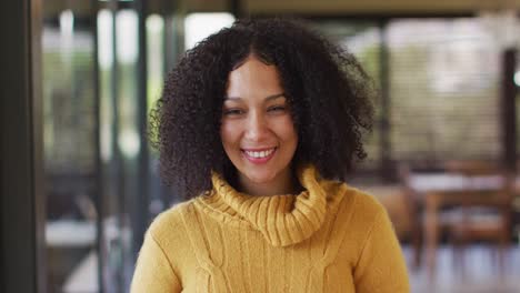 Portrait-of-happy-mixed-race-woman-sitting-in-living-room,-smiling-and-laughing-to-camera