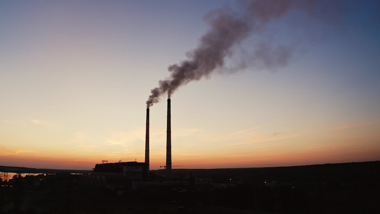 Dark background of plant with industrial pipes. Smokestacks of the plant against the background of an orange sunset. Bad ecological situation. Air pollution.