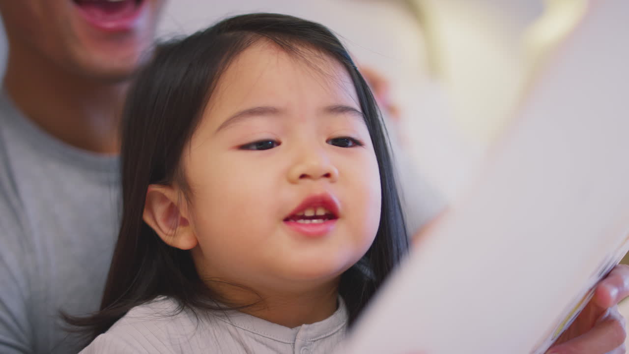 집 에서 딸 과 함께 이야기 를 읽고 있는 아버지 와 함께 침대 에 누워 있는 가족 의 가까운 모습