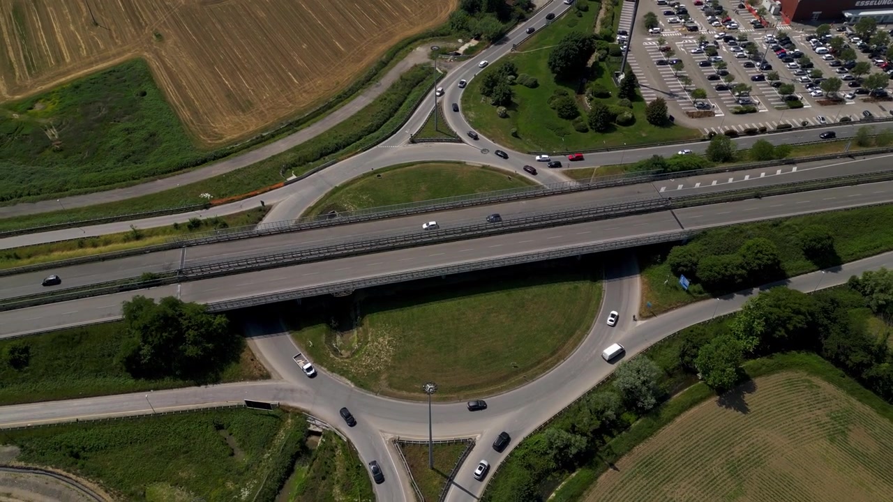 Vista aerea con drone di un trafficato incrocio a rotatoria su una strada provinciale nel nord Italia. Il movimento continuo dei veicoli mostra una moderna infrastruttura di trasporto e una rete stradale.