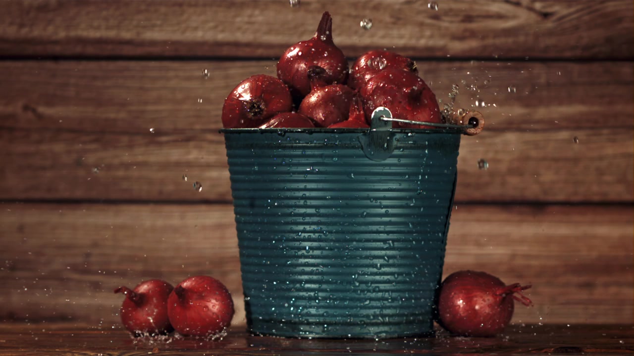 Frische rote Zwiebeln in einem Eimer mit spritzendem Wasser auf rustikalem Holzhintergrund.