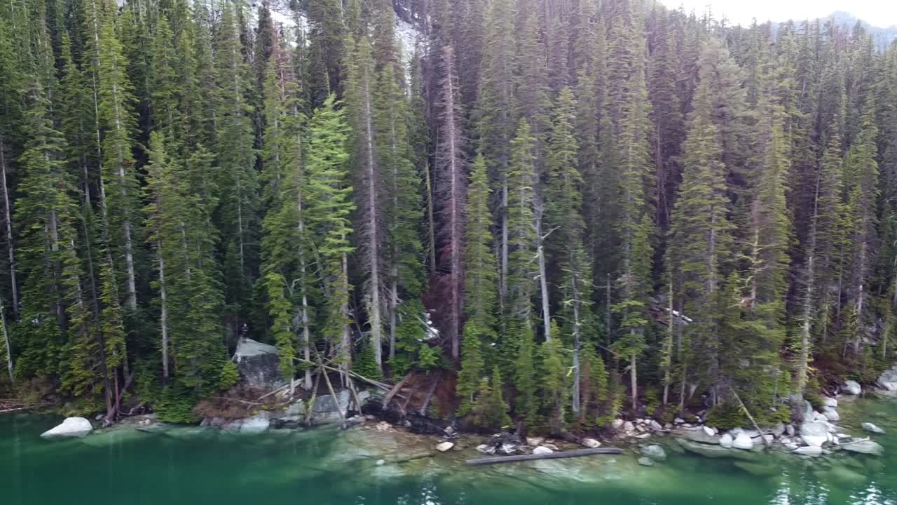 panorámica izquierda toma de drones de la rocosa costa alpina del lago y bosque colchuck, cerca de los encantos en la cordillera de las cascadas de washington