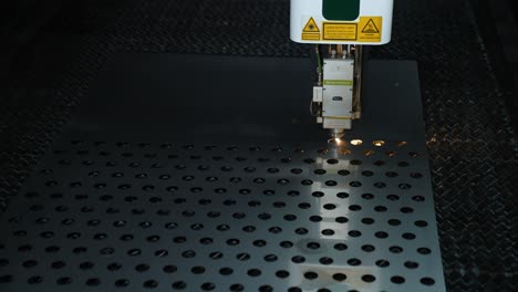 cnc machine cuts holes with a laser in a sheet of metal. sparks from the laser. automatic cutting at an industrial plant