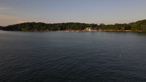 Birds-soaring-over-lake-during-warm-summer-afternoon-in-new-england,-northeast-USA,-with-a-marina-and-green-trees