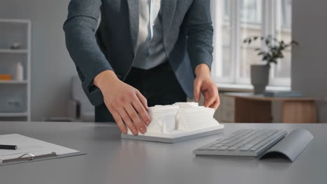 A professional placing a 3D printed architectural model on an office desk