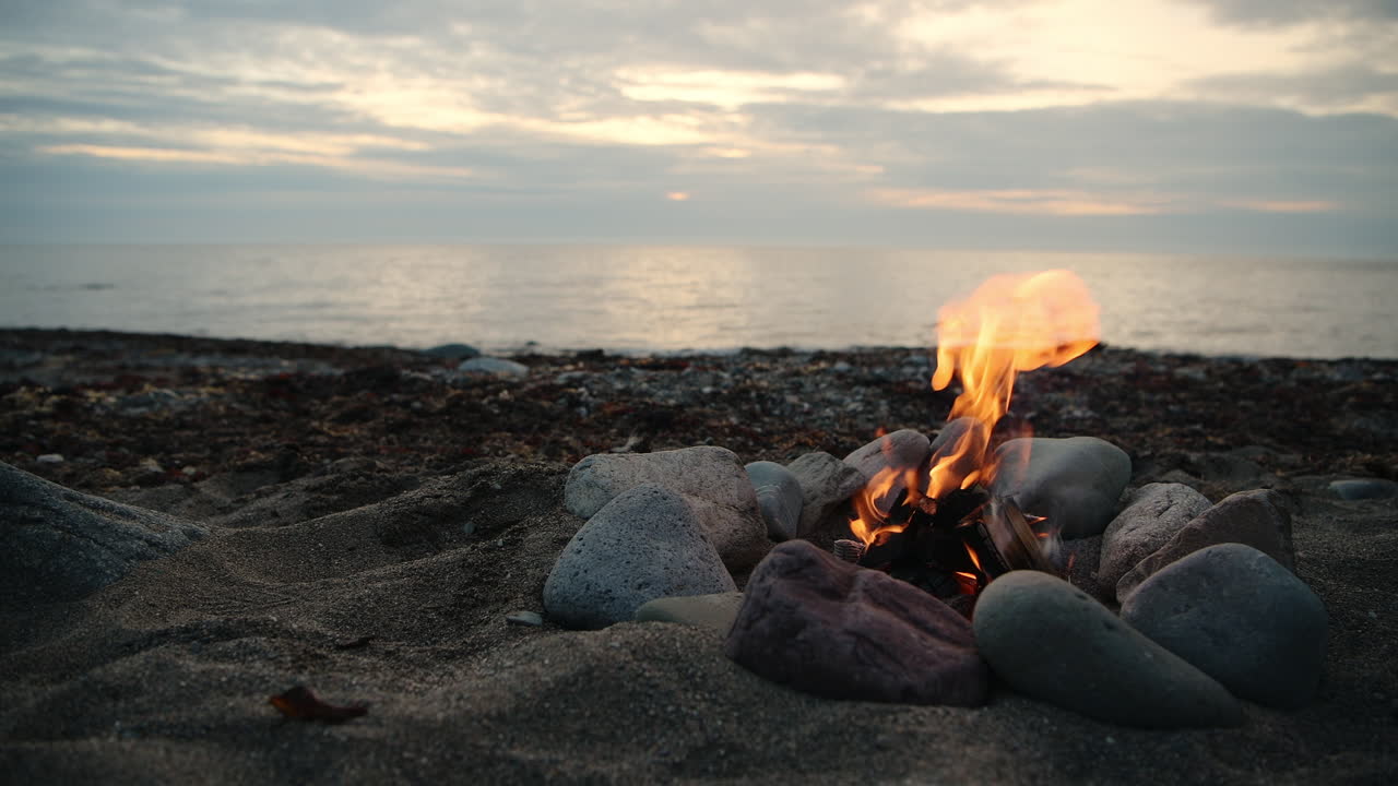 Wild camping on the beach - Small campfire bonfire surrounded by rocks on shore in Wales during outdoor adventure camping trip